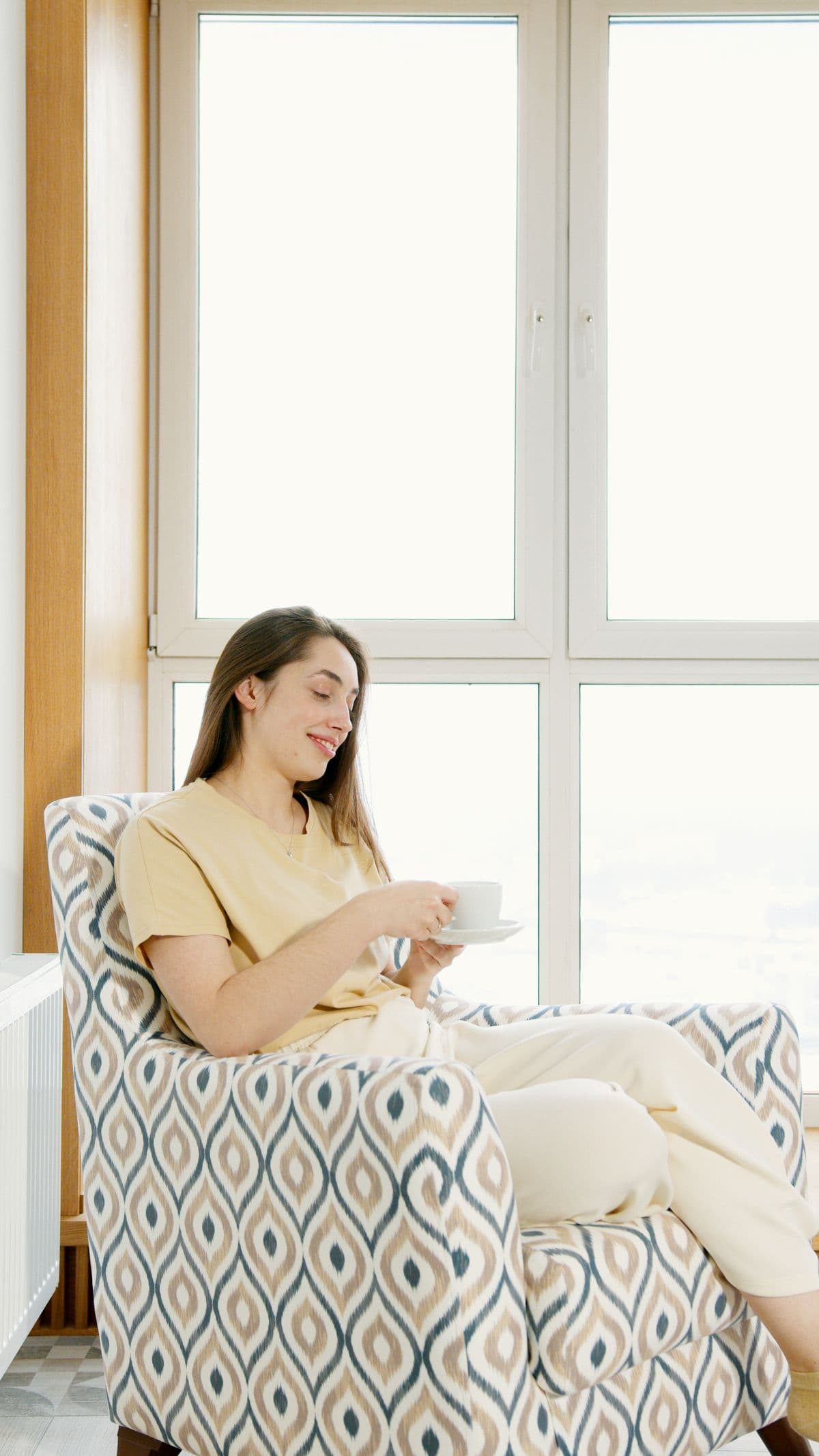A woman relaxing with a cup of coffee by a sunlit window